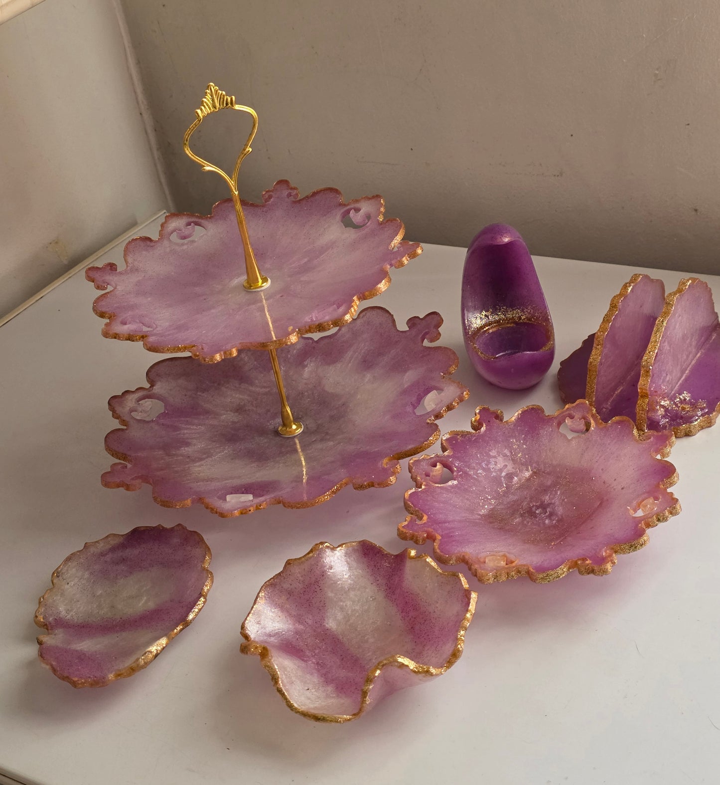 Purple resin flower petal serving trays with gold glitter edges and a gold metal stand, displayed on a white surface with a beige background.