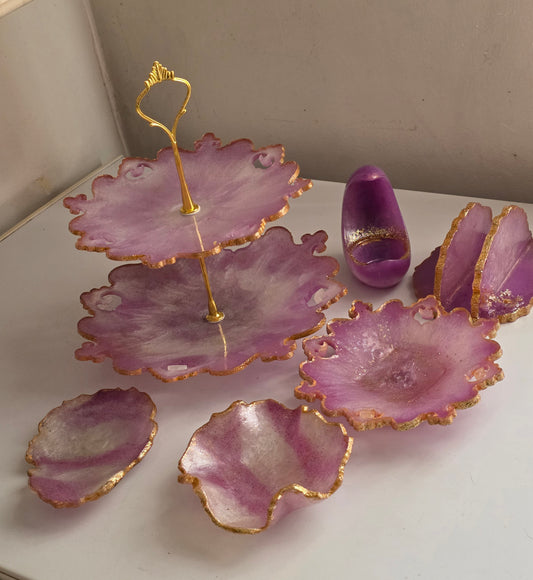 Purple resin flower petal serving trays with gold glitter edges and a gold metal stand, displayed on a white surface with a beige background.